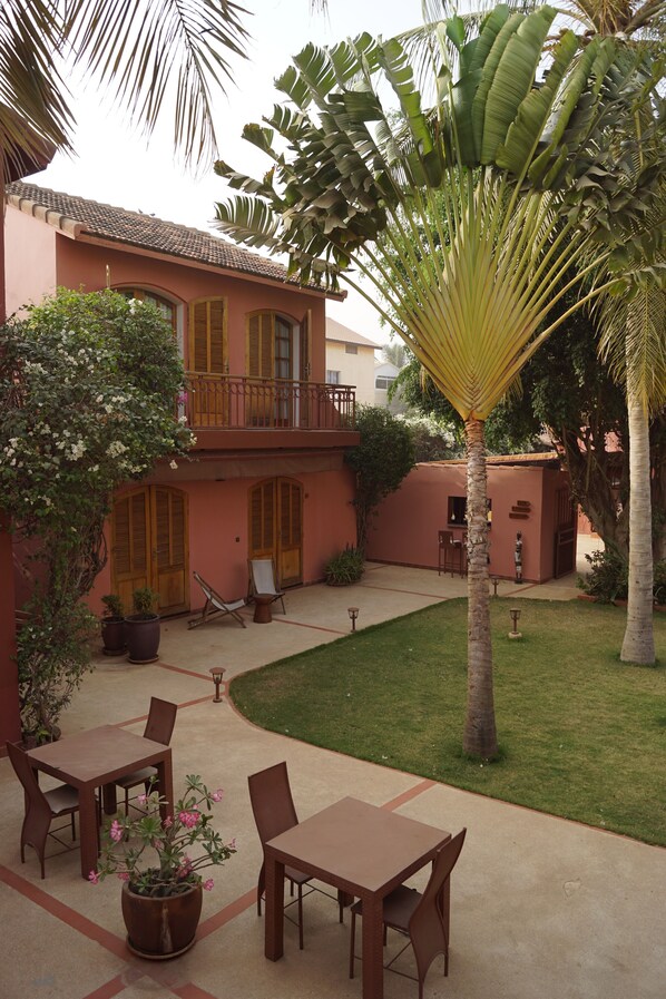 A courtyard with a dining area, a small building, and a palm tree. - Les Goréennes Suites (Mbour)