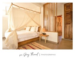 Quarto com cama de dossel, mesa de cabeceira com luminária e tapete estampado.