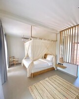 Una camera da letto con un letto a baldacchino, una piccola sedia di legno, un comodino con una lampada e un tappeto decorato.