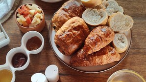 A breakfast setting with croissants, fruit, coffee, and juice on a wooden table. - Les Goréennes Suites (Mbour)