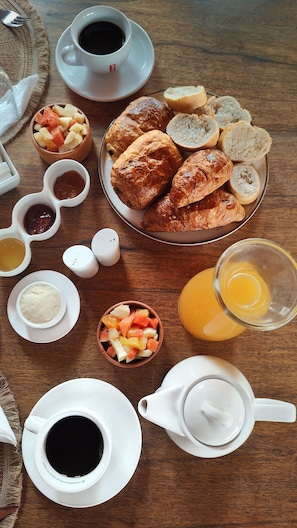 Un desayuno con cruasanes, fruta, café y jugo sobre una mesa de madera.