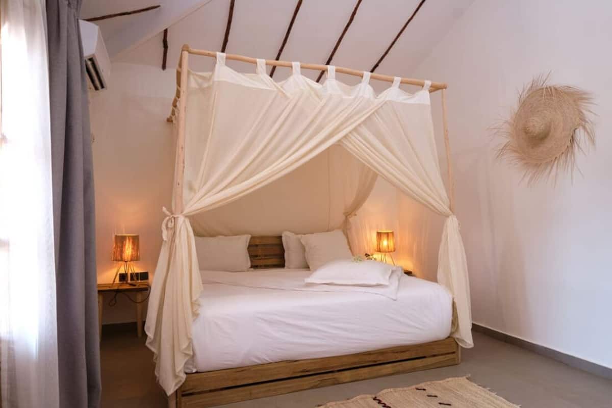 Ein Bett mit Baldachin, Nachttischlampen und einem Strohhut an der Wand.