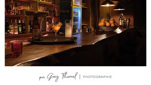 A bar area with shelves of liquor bottles, a refrigerator, and a bar counter with glasses and a cocktail. - Les Goréennes Suites (Mbour)