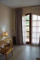 Una habitación con escritorio de madera, lámpara, silla y puerta que da a un espacio exterior con vistas a zonas verdes.
