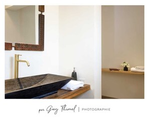 Une salle de bain moderne avec un lavabo en granit foncé, un robinet doré et une étagère en bois sur laquelle sont posés une serviette et un petit vase.
