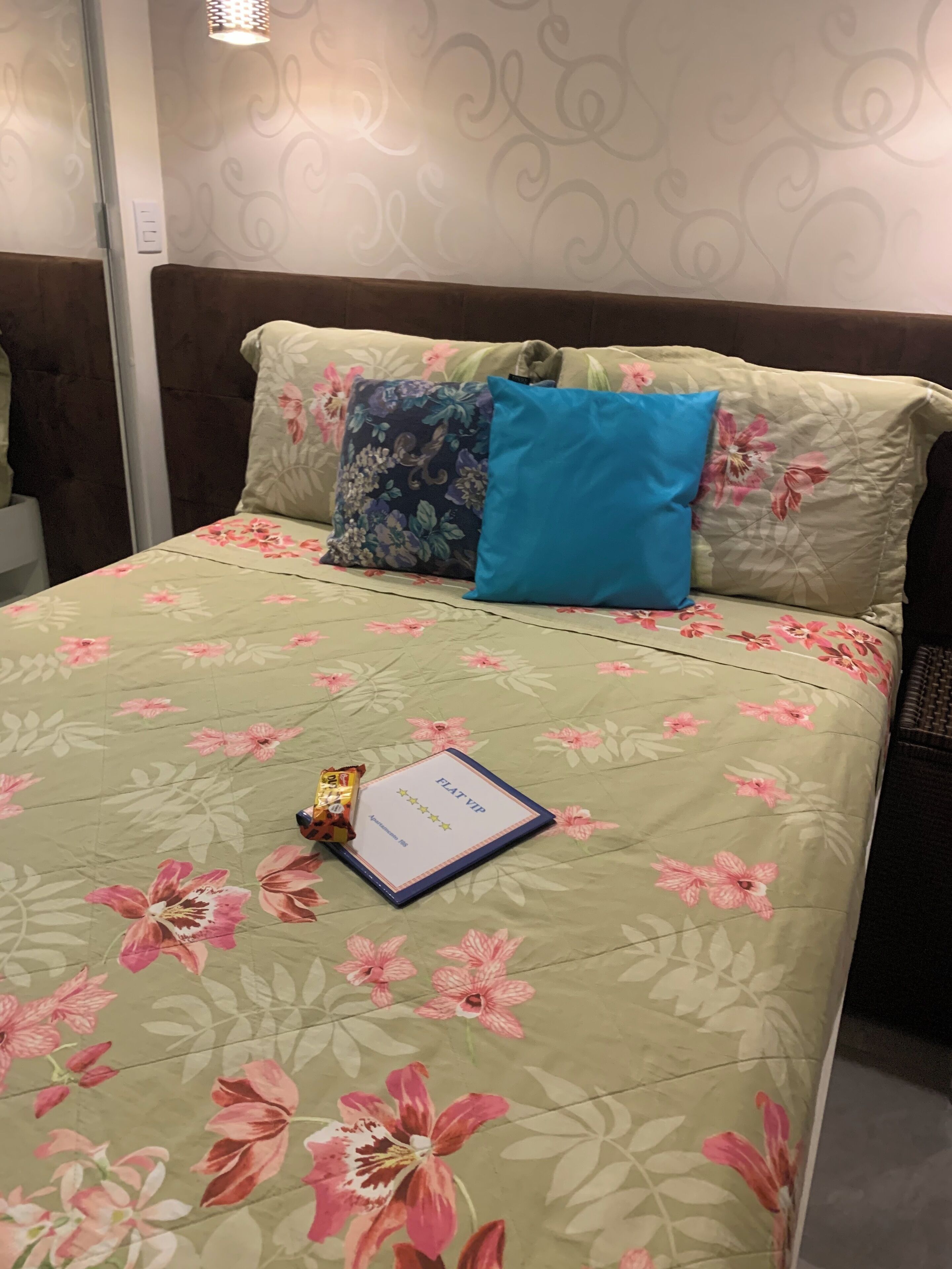 A bed with floral bedding, a blue pillow, and a booklet on the bed.