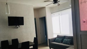 Una sala de estar con un sofá gris, un televisor montado en la pared y un ventilador de techo.