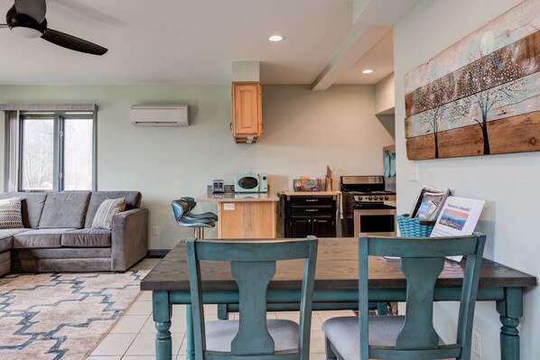 A modern living room with a sofa, a dining table with chairs, a kitchen area, and a ceiling fan.