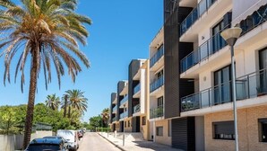 A modern multi-story residential building with balconies, a clear sky, and palm trees along the street. - Alojamento Santa Maria B4 1E (Tavira)