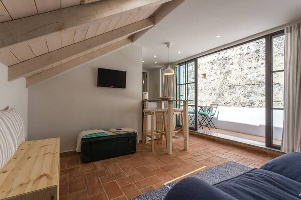 A modern room with a sloped ceiling, a large window, a television, and a seating area with a sofa and chairs.