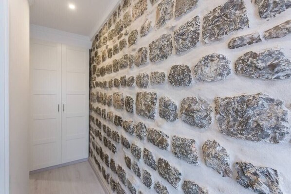 A hallway with a textured stone wall and white cabinets.