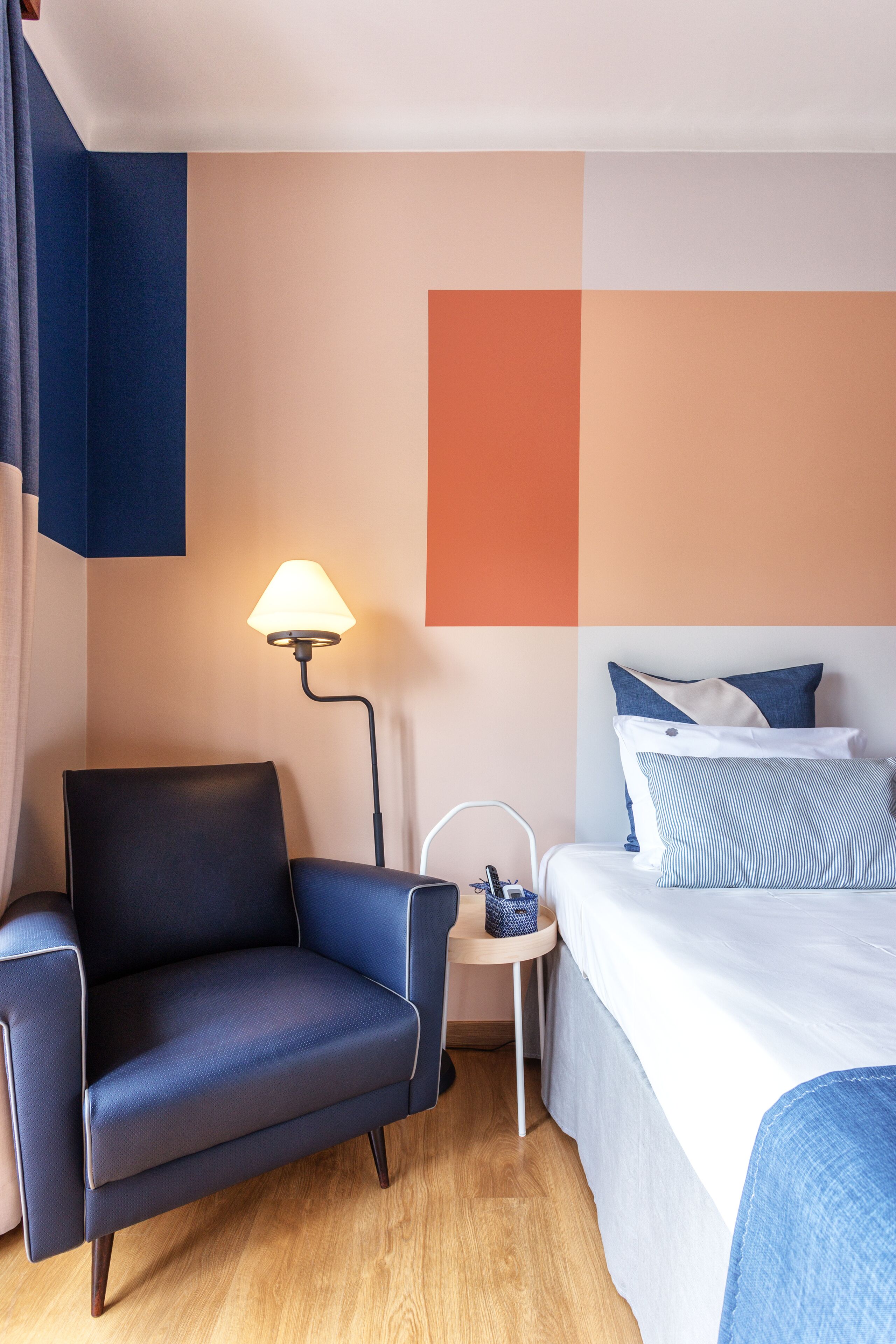 Una habitación de hotel con cama, una silla, una lámpara y una mesita.