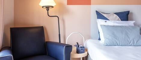 Una habitación de hotel con cama, una silla, una lámpara y una mesita.