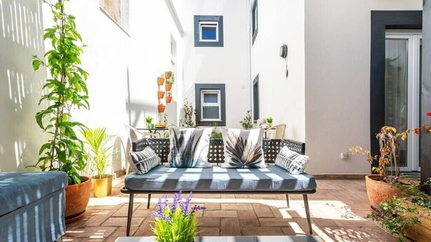 Un patio iluminado por el sol con un sofá, plantas en macetas y una mesa.