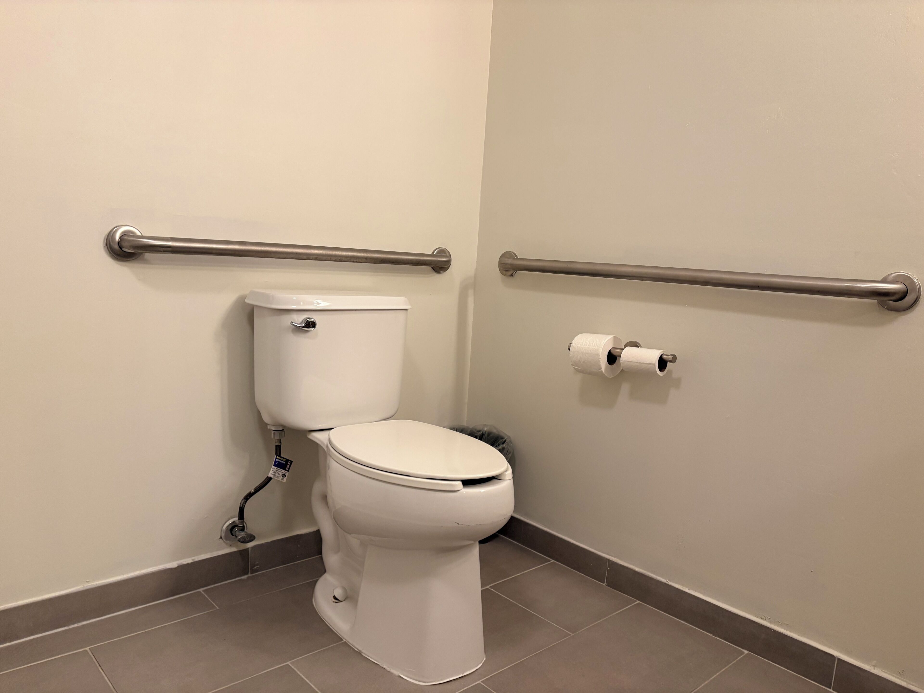 A standard bathroom with a toilet, grab bars, and a toilet paper holder.