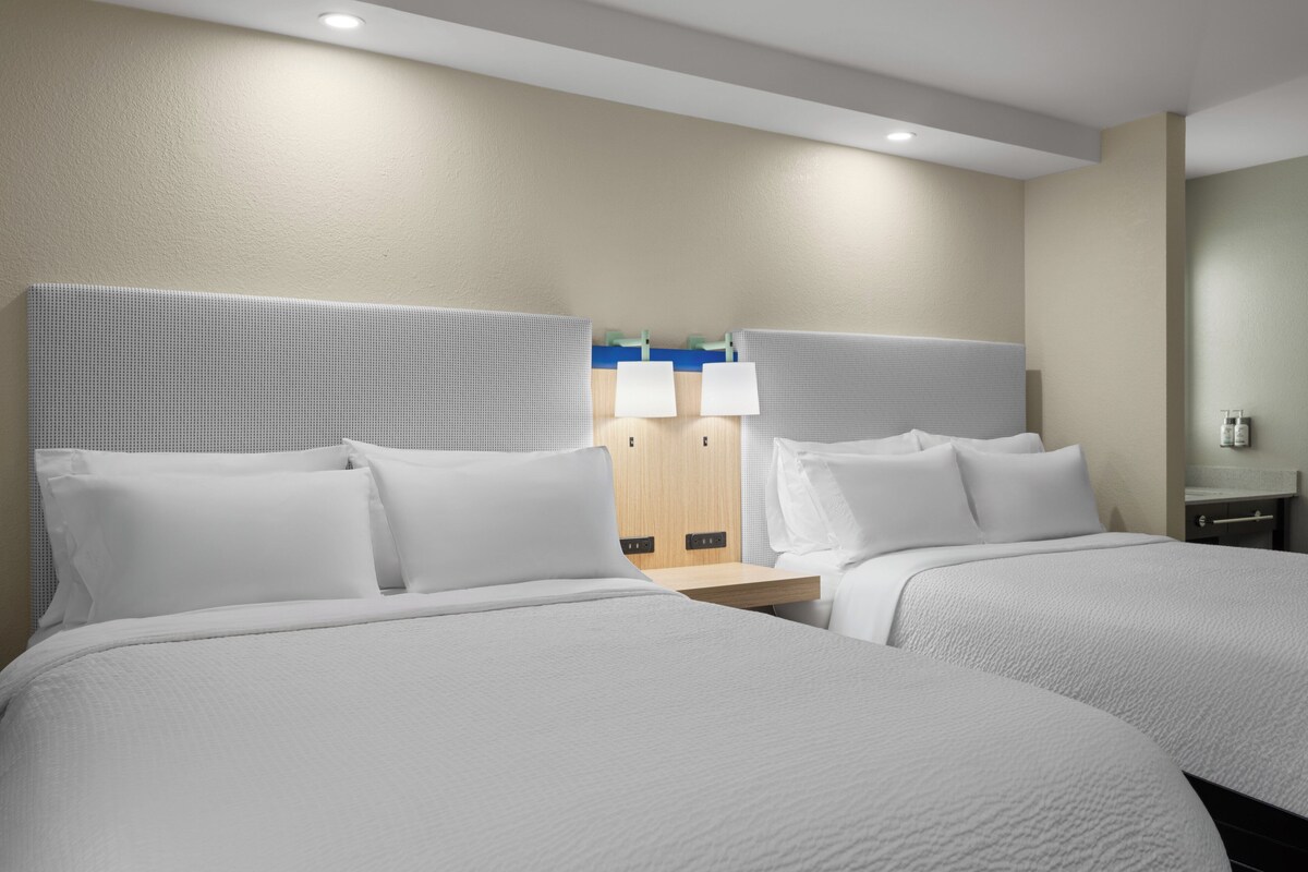 Ein Hotelzimmer mit zwei Betten, einem Holzschrank und einem Nachttisch mit Lampe.