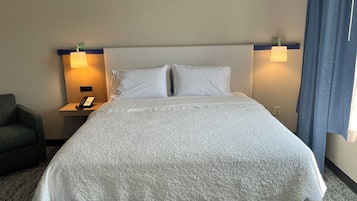 Een hotelkamer met een groot bed, twee bedlampen, een telefoon en een stoel.