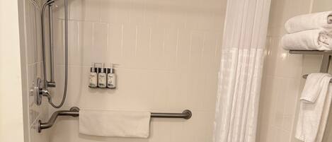 A shower area with a grab bar, a white towel rack, and a shower curtain.