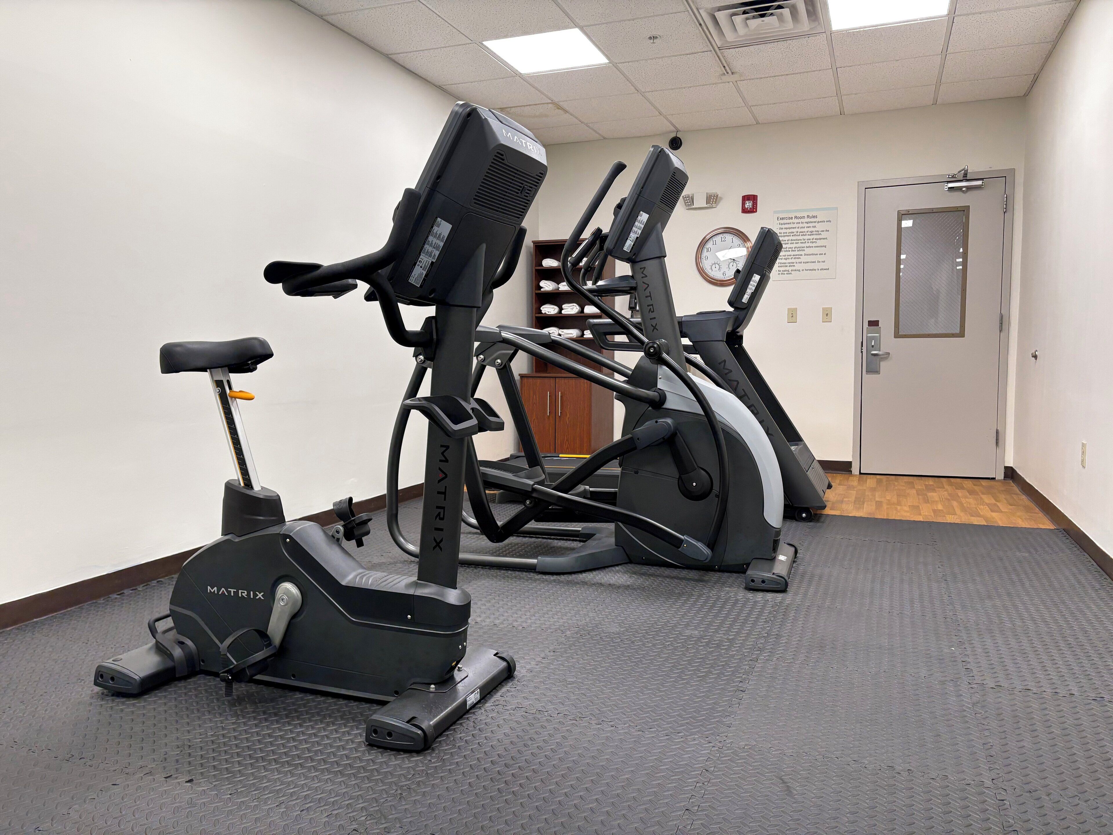 A fitness room with two treadmills, a stationary bike, and a mat.