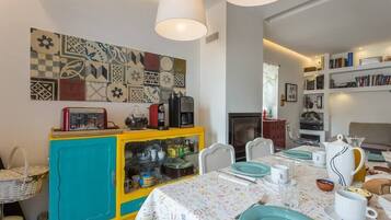 Un comedor con una mesa preparada para cuatro personas, un armario amarillo y azul con utensilios de cocina, y una pared con un colorido diseño de azulejos.