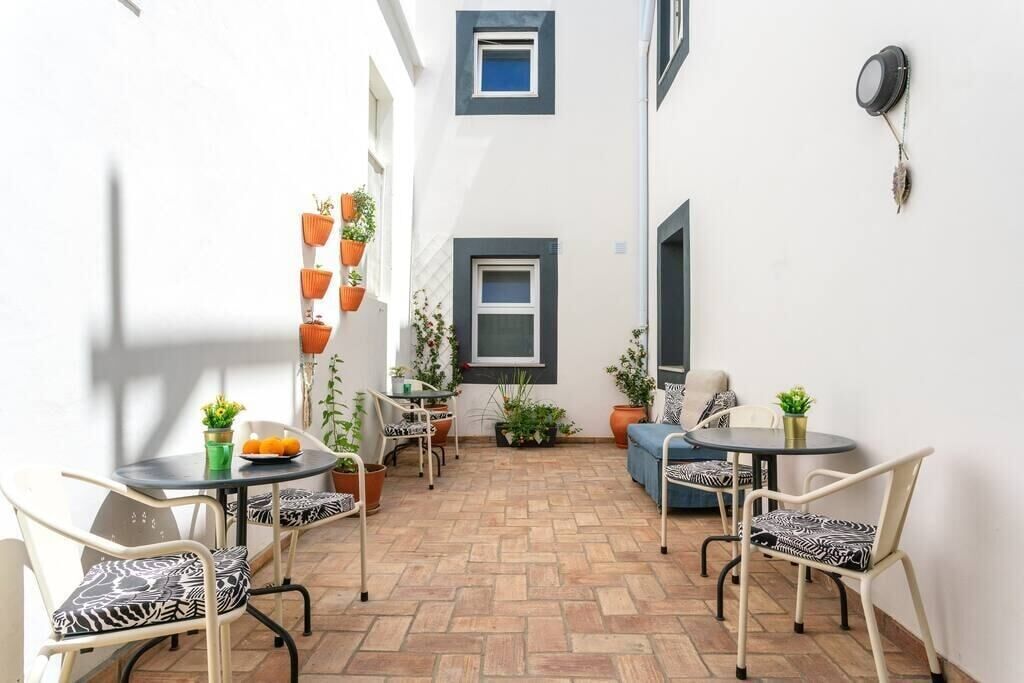 A small patio area with two round tables and four chairs, each with zebra-patterned cushions. There are potted plants on the walls and a small table with a bowl of fruit.