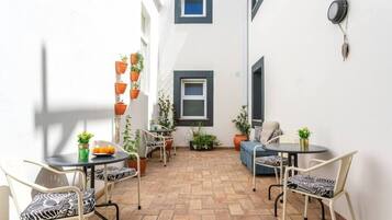 A small patio area with two round tables and four chairs, each with zebra-patterned cushions. There are potted plants on the walls and a small table with a bowl of fruit.