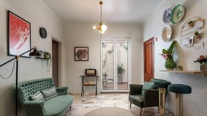 A living room with a green sofa, a round rug, and a coffee table. There is a television on a stand, a plant, and a door leading to a balcony.