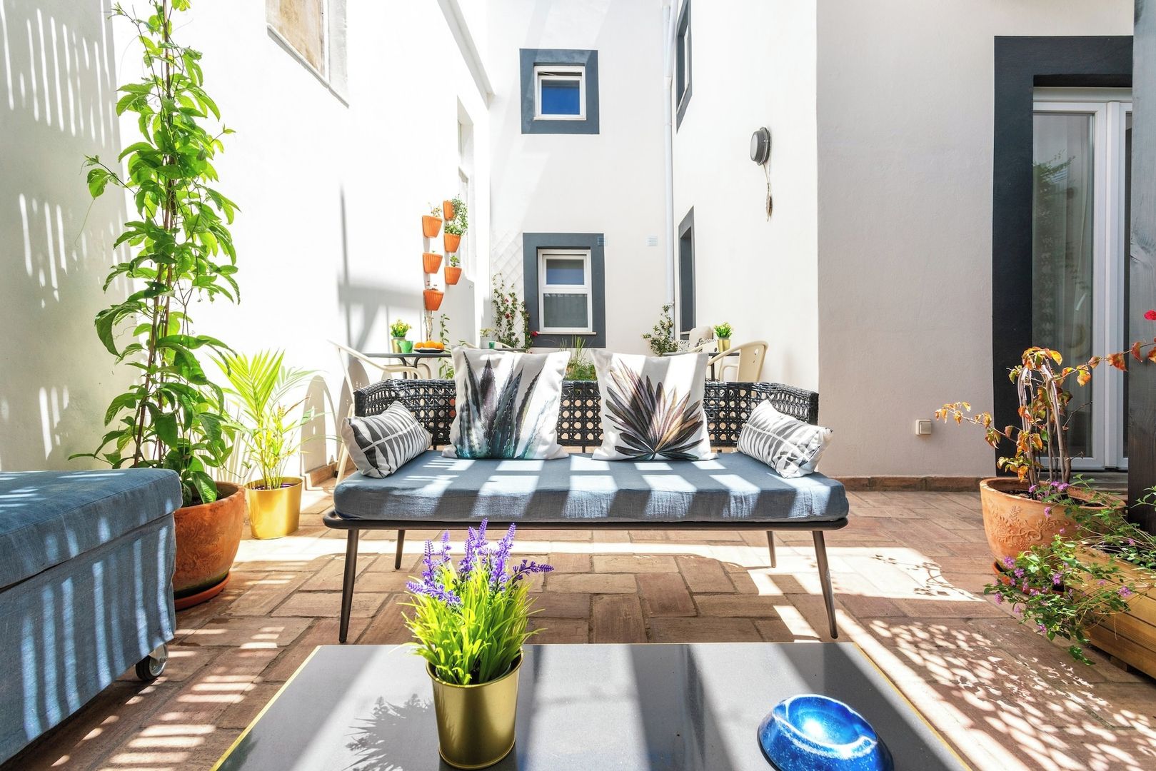Un patio soleado con sofá, plantas en macetas y una pequeña mesa.