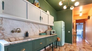 A kitchen with a marble countertop, green cabinets, a white refrigerator, and a microwave.
