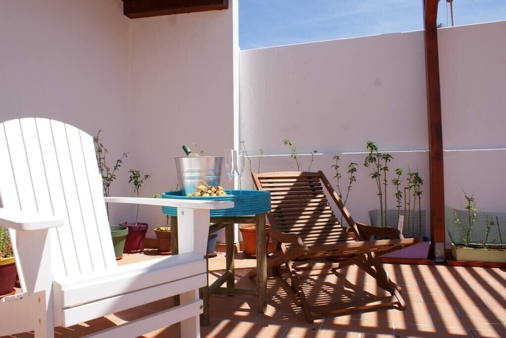 Un patio con una silla blanca, una mesa de madera y plantas en macetas.
