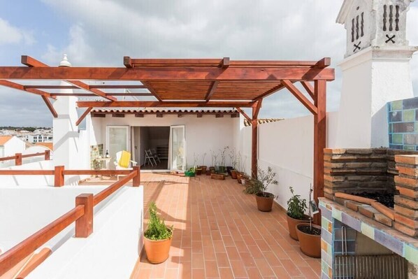 Eine Dachterrasse mit einer Holzpergola, Topfpflanzen und einem Kamin aus Stein.