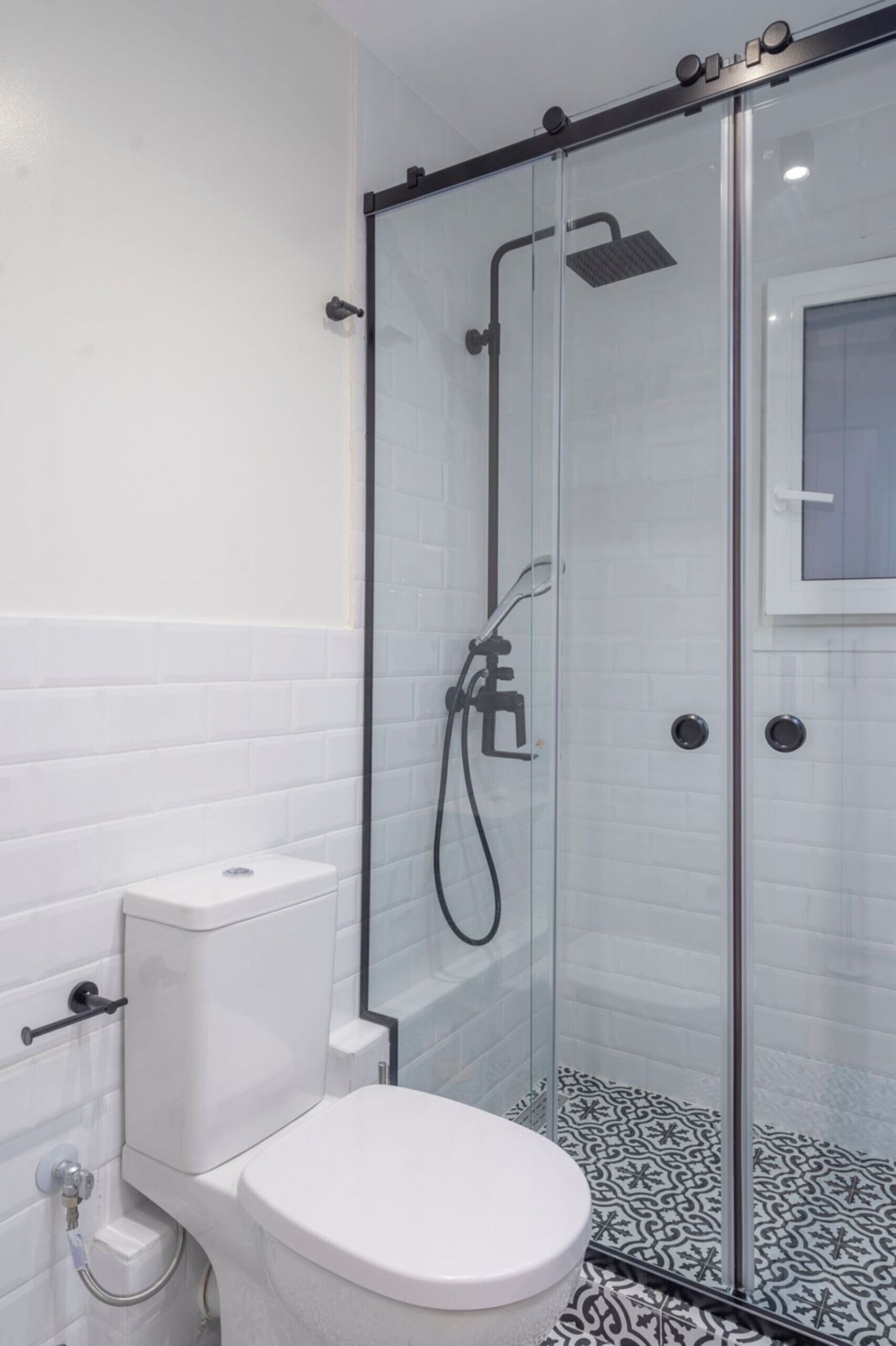 A modern bathroom with a glass-enclosed shower, white tiled walls, and a white toilet.