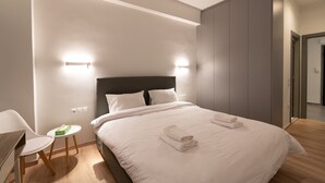 Moderni hotellihuone, jossa on suuri sänky, kaksi yöpöytävalaisinta, pieni pyöreä pöytä ja tuoli.