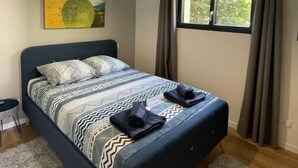 Un dormitorio con cama, luz de techo, ventana con cortinas y un cuadro en la pared.