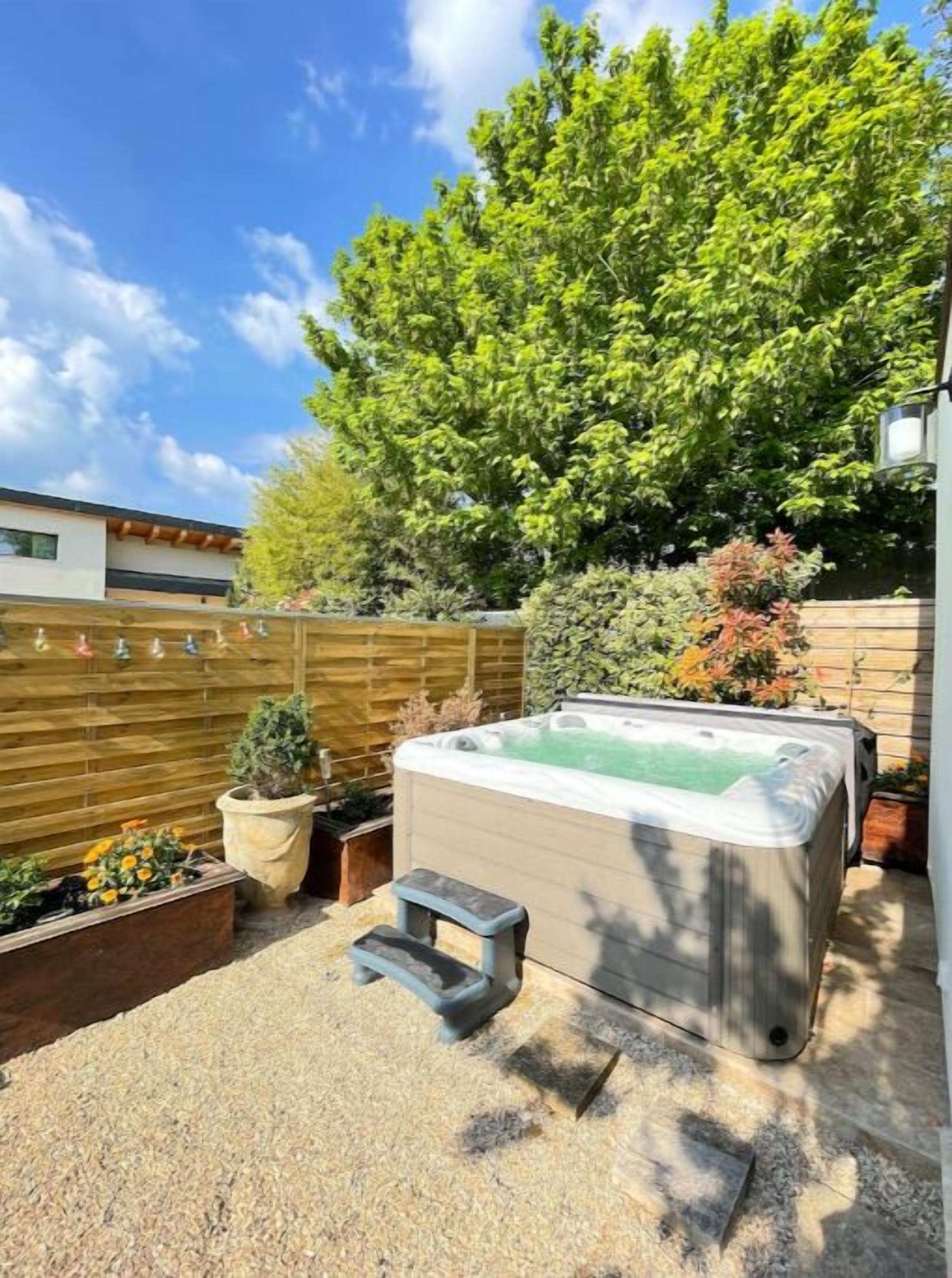 Un bain à remous dans un jardin, avec une clôture en bois, des plantes en pot et une terrasse en bois.