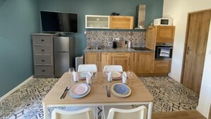 Cocina compacta con una mesa de comedor para dos personas, un televisor montado sobre la encimera y un microondas en la superficie.