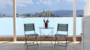 Un espace extérieur aménagé avec une zone de repos couverte, comprenant deux chaises et une table, offrant une vue sur une marina et des collines lointaines.