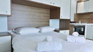 Une chambre d’hôtel moderne avec un grand lit, du linge de lit blanc, une tête de lit en bois et un four encastré.