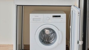Un lave-linge Siemens compact et blanc, installé dans un petit espace clos, avec vue sur le paysage urbain et les antennes en arrière-plan.