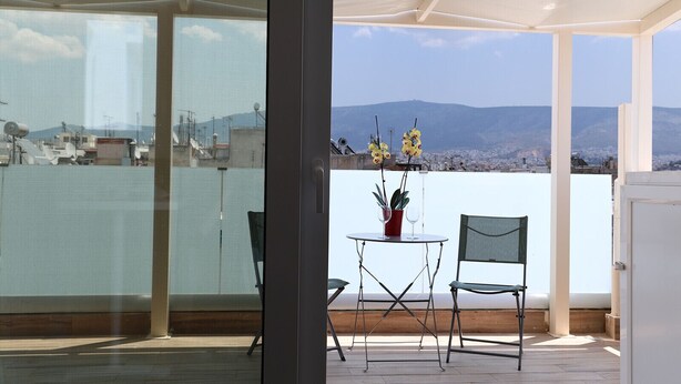 Un balcon avec une table et des chaises, un pot de fleurs et une vue sur le paysage urbain et les montagnes.