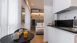 A compact hotel room with a kitchenette, a dining area with breakfast items, and a bed with a headboard.
