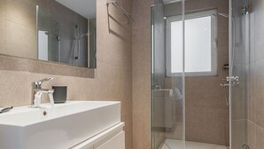 A modern bathroom with a glass-enclosed shower, a white sink, and a large mirror.