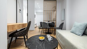 Una sala de estar moderna con una mesa redonda negra, un sofá gris y un escritorio de madera con una silla.