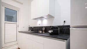 Una cocina moderna con armarios blancos, encimera de mármol negro y cafetera integrada.