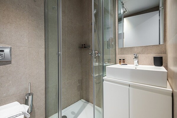 A modern bathroom with a glass shower enclosure, a white sink, and a large mirror.