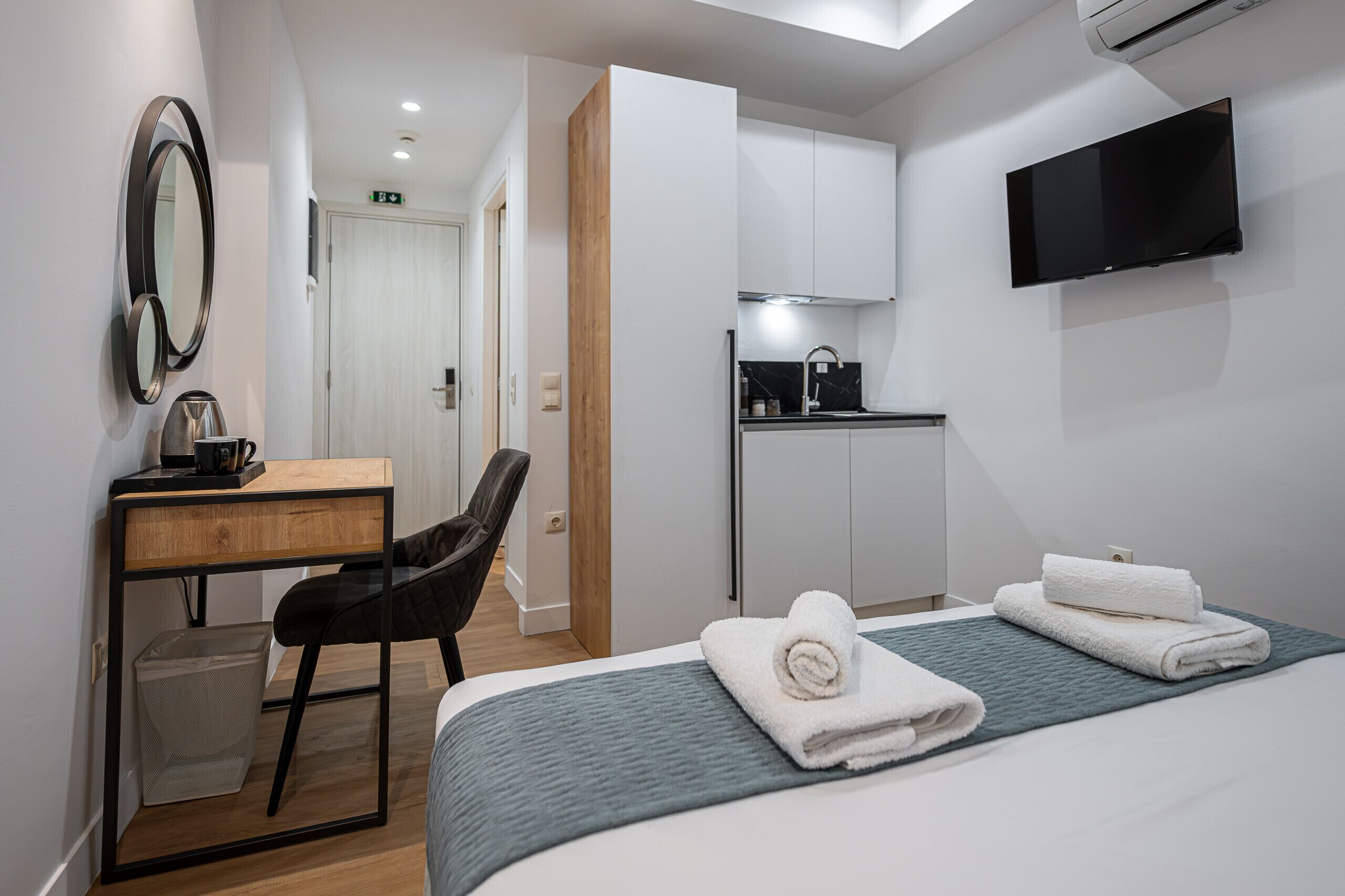 A hotel room with a bed, a desk, a chair, a TV, and a kitchenette.