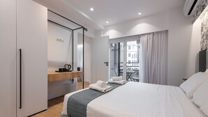 Ein modernes Hotelzimmer mit einem großen Bett, einem Schreibtisch mit Computer, einem Sessel und einem Balkon mit Blick.