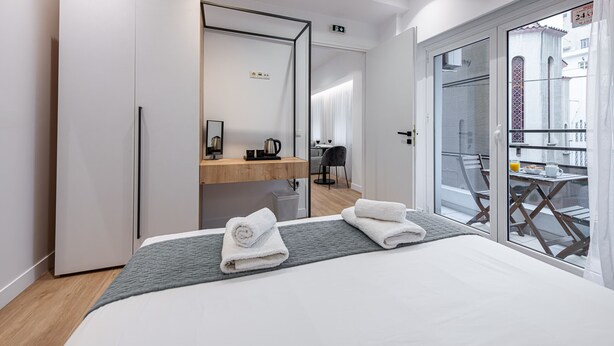 Ein modernes Hotelzimmer mit einem großen Bett, einem Holfnachtkästchen, einem Spiegel und einem Balkon mit Tisch und Stühlen.