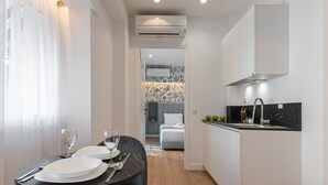 A modern hotel room with a dining area, kitchenette, and a bedroom with a patterned wallpaper. - Kriel Suites by LIV Homes 201 (Athens)