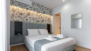 A modern hotel room with a large bed, grey headboard, floral wallpaper, and a mirror on the wall. - Kriel Suites by LIV Homes 201 (Athens)